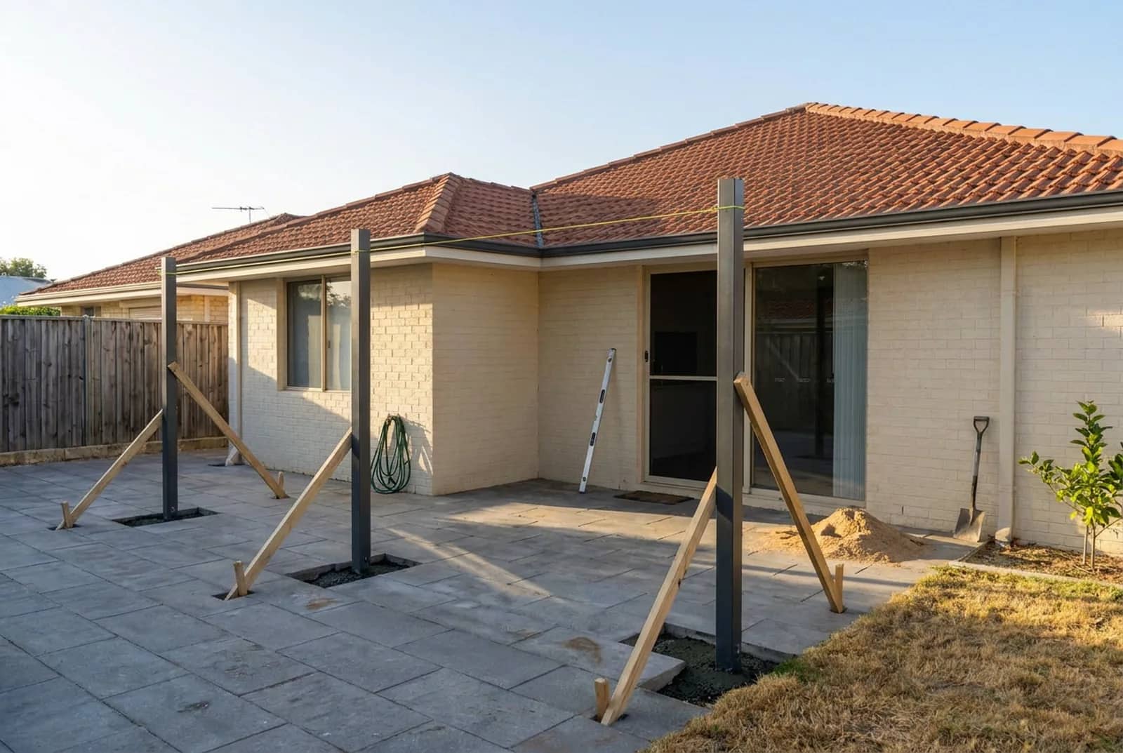 The same Perth backyard with the steel posts standing plumb in fresh concrete footings, held upright by temporary timber braces
